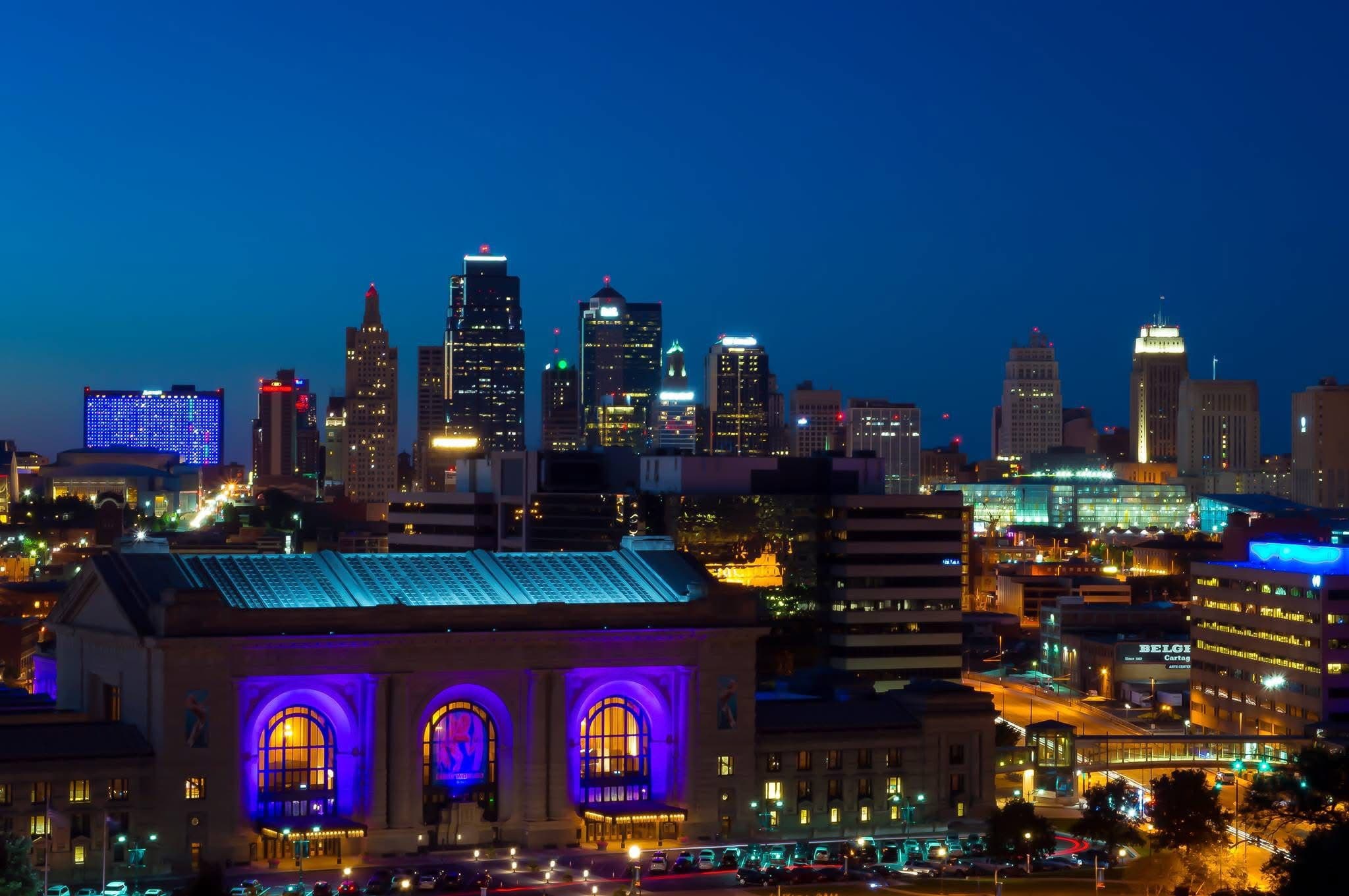 Downtown Kansas City at dusk, seen from the south: Union Station lit purple in the foreground with the skyline behind it.